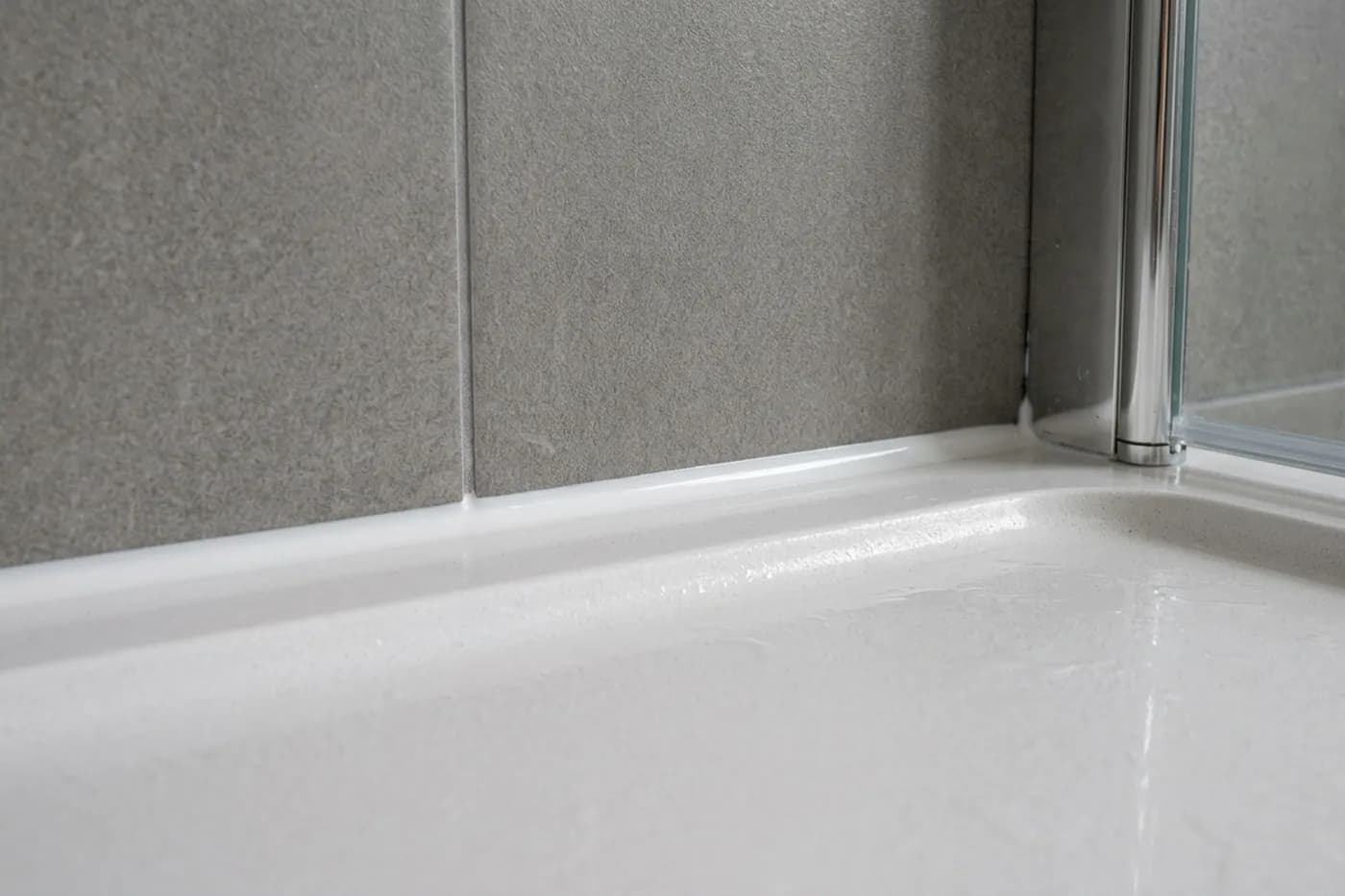 The joint between a shower tray and grey wall tiles carrying a fresh white silicone bead tooled to a clean concave finish