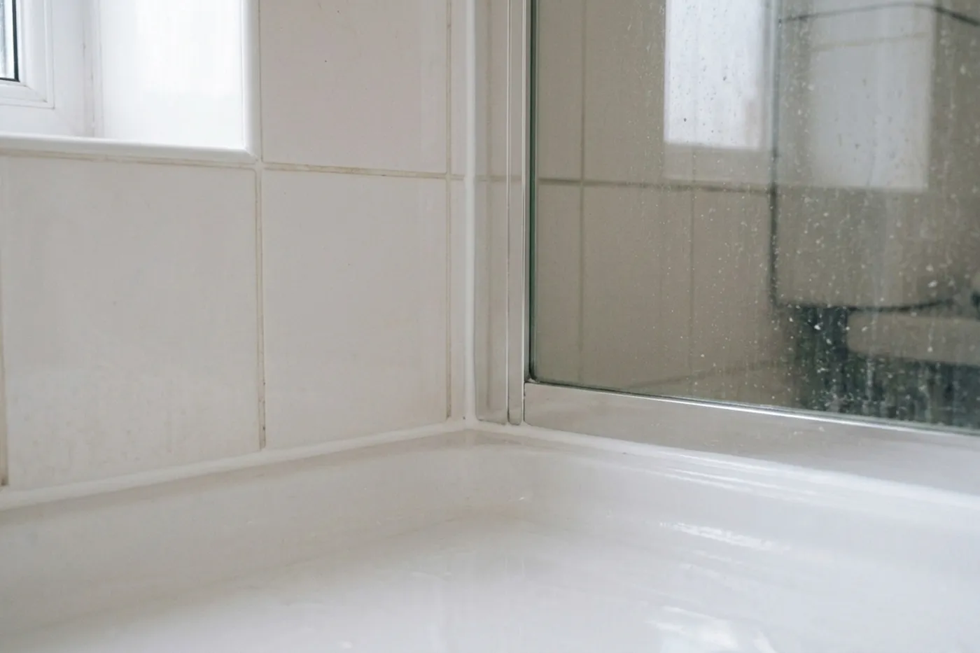 The same shower corner after resealing, with a clean white bead at the tray edge and up the corner and the glass screen foot clear